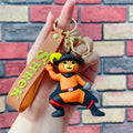 Puss in Boots 3D PVC keychain in musketeer pose with brown Shrek branded wrist strap, held in hand against brick wall