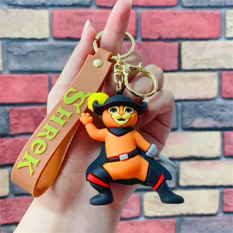 Puss in Boots 3D PVC keychain in musketeer pose with brown Shrek branded wrist strap, held in hand against brick wall
