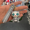 Grey Cheshire Cat 3D PVC keychain with teal eyes and grey Alice in Wonderland wrist strap, held in hand