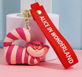 Cheshire Cat 3D PVC keychain with pink and magenta stripes and red Alice in Wonderland wrist strap on pink surface